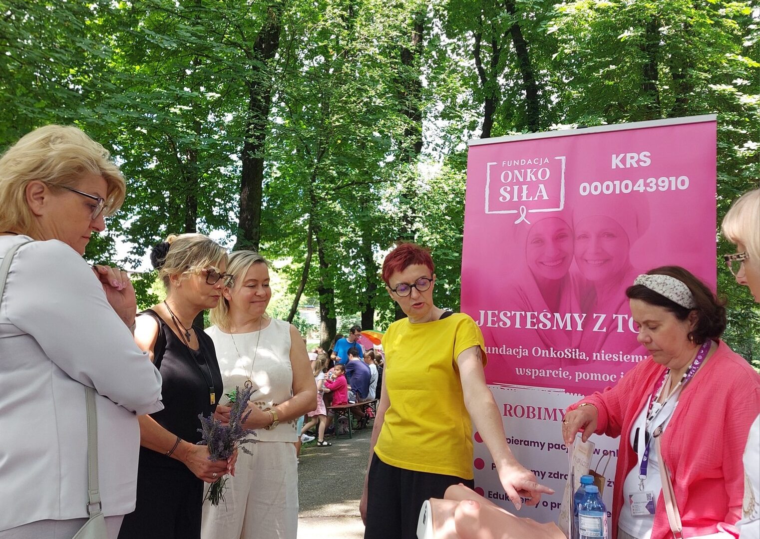 Plenerowa akcja profilaktyczna Fundacji ONKOSIŁA. Zdjęcie przedstawia grupę kobiet stojących przy stoisku Fundacji z edukacyjnymi modelami piersi.