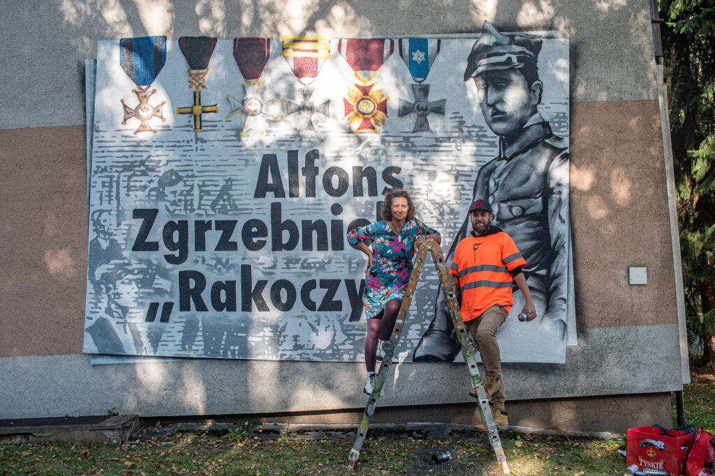 Prezeska Fundacji Tacy Jesteśmy przed muralem poświęconym Alfonsowi Zgrzebniokowi.