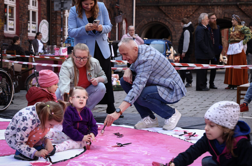 Kadr z wydarzenia SPINAKCJA. Dzieci i osoby dorosłe malujące różowego ślimaka - symbol Fundacji.