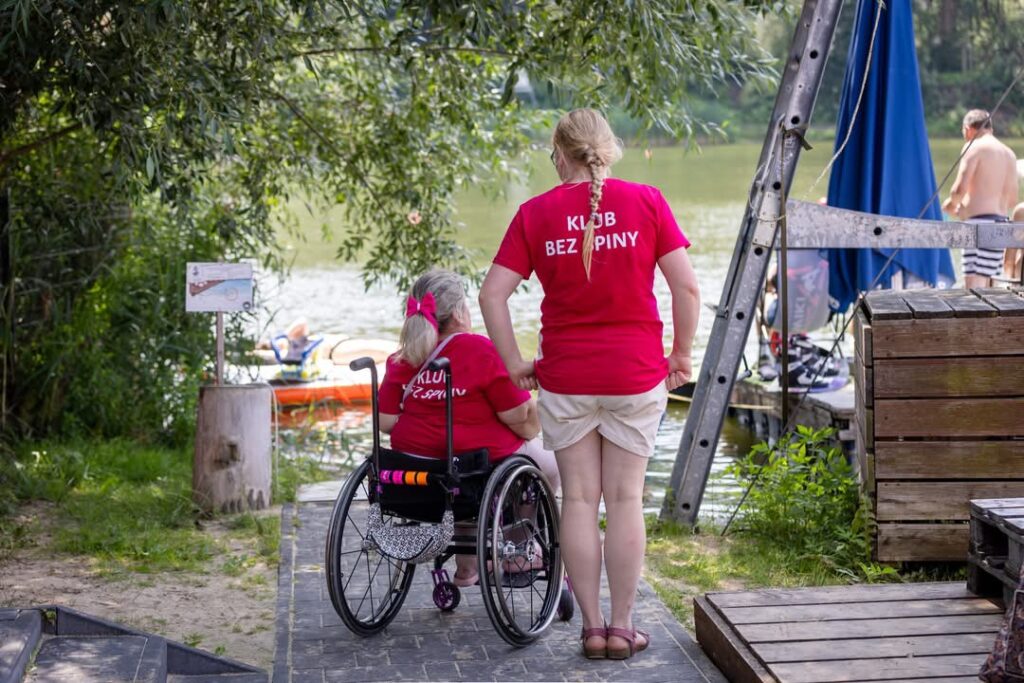 Osoba dorosła z rozszczepem kręgosłupa z wolontariuszką w koszulkach z napisem "KLUB BEZ SPINY".